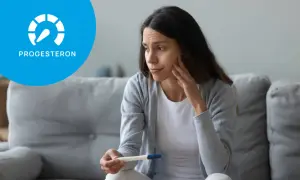 Zmartwiona kobieta trzyma test ciążowy, zastanawiając się nad objawami niskiego progesteronu.