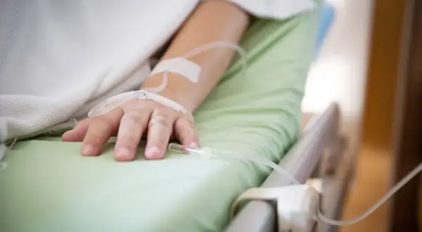 Ręka pacjenta w szpitalnym łóżku z wenflonem, walczącego z infekcją, np. Klebsiella pneumoniae.