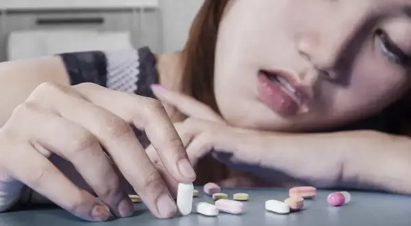 Kobieta z opuszczoną głową sięga po tabletki. Wokół niej rozsypane leki, które wymagają szczególnej atencji.
